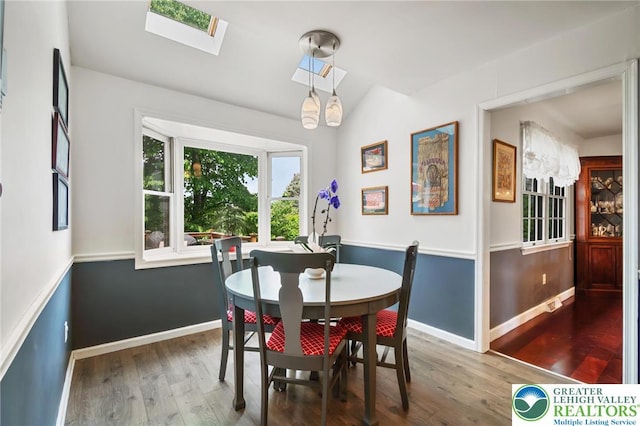 dining area featuring wood finished floors, a skylight, baseboards, and lofted ceiling