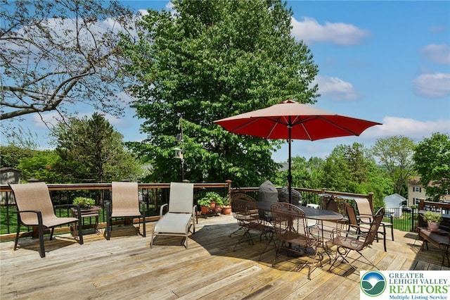wooden terrace featuring outdoor dining space and view of wooded area