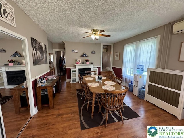 dining area featuring a glass covered fireplace, ceiling fan, a textured ceiling, wood finished floors, and an AC wall unit