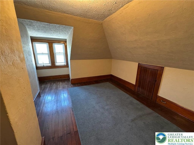 additional living space with a textured ceiling, dark wood finished floors, lofted ceiling, and baseboards