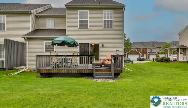 rear view of property with a deck, a lawn, and roof with shingles