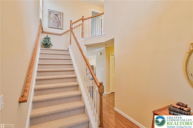 staircase with wood finished floors, a high ceiling, and baseboards