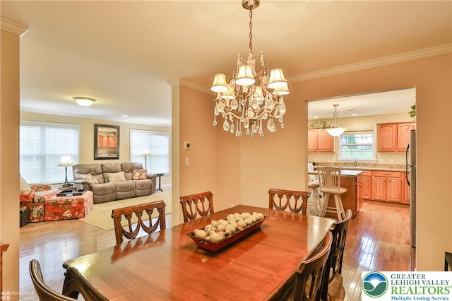 dining area featuring light wood-style floors, plenty of natural light, crown molding, and a chandelier