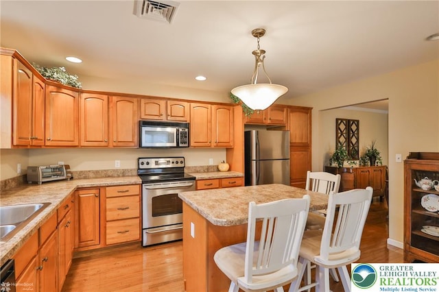 kitchen featuring stainless steel appliances, a breakfast bar, a center island, light countertops, and hanging light fixtures