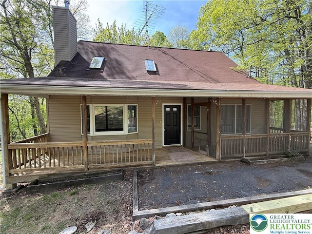 view of front of property featuring a chimney, covered porch, and a sunroom