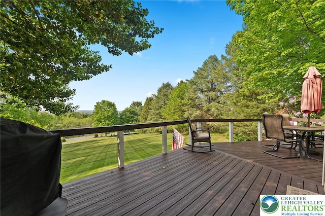 wooden terrace featuring outdoor dining space, a grill, and a lawn