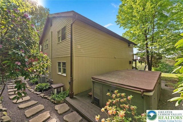 view of home's exterior featuring a hot tub, a wooden deck, and central AC
