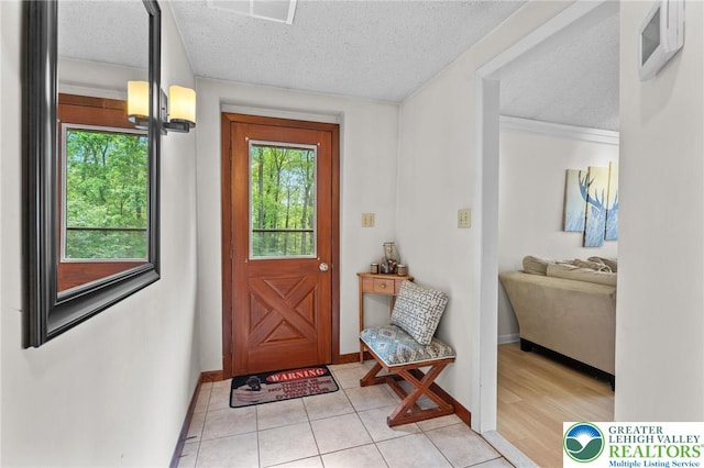 doorway to outside featuring plenty of natural light, a textured ceiling, baseboards, and light tile patterned floors