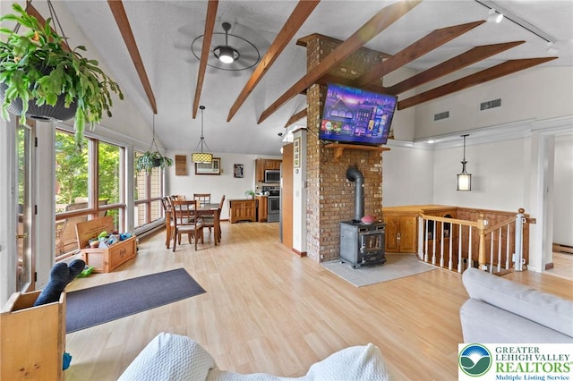 living room with beam ceiling, a wood stove, wood finished floors, track lighting, and high vaulted ceiling