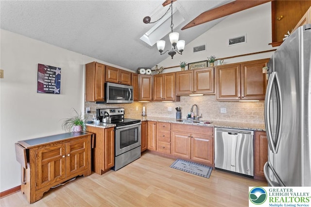 kitchen with appliances with stainless steel finishes, a sink, lofted ceiling, tasteful backsplash, and light stone countertops