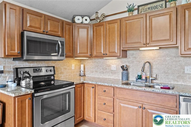 kitchen featuring stainless steel appliances, a sink, light stone countertops, brown cabinets, and a textured ceiling
