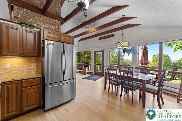 kitchen featuring freestanding refrigerator, beamed ceiling, decorative backsplash, plenty of natural light, and light stone counters