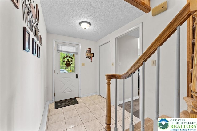 entryway with a textured ceiling, baseboards, stairway, and light tile patterned floors