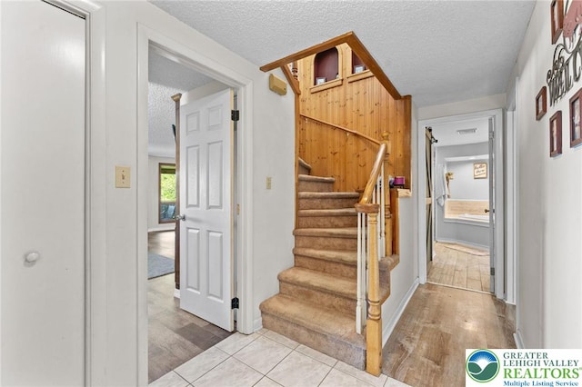 stairway with a textured ceiling, wood finished floors, and baseboards