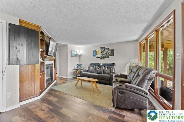 living area featuring a textured ceiling, dark wood finished floors, a glass covered fireplace, and baseboards