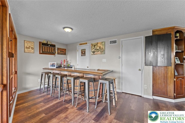 indoor bar featuring dark wood-style flooring, a textured ceiling, and baseboards