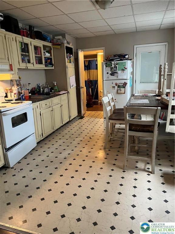 310 E Broad St, Tamaqua Borough, PA 18252 - kitchen with white appliances, a paneled ceiling, cream cabinetry, glass insert cabinets, and light flooring