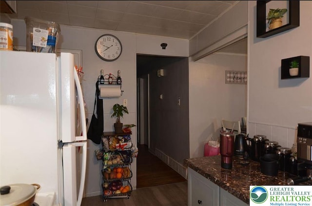 kitchen featuring freestanding refrigerator, dark wood-style flooring, and dark stone counters