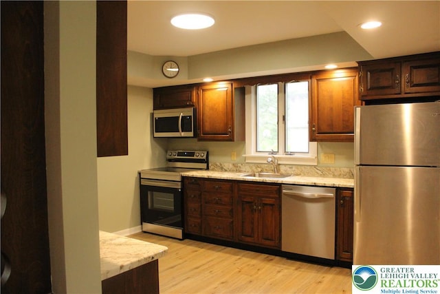 kitchen with stainless steel appliances, a sink, light wood finished floors, light stone counters, and recessed lighting