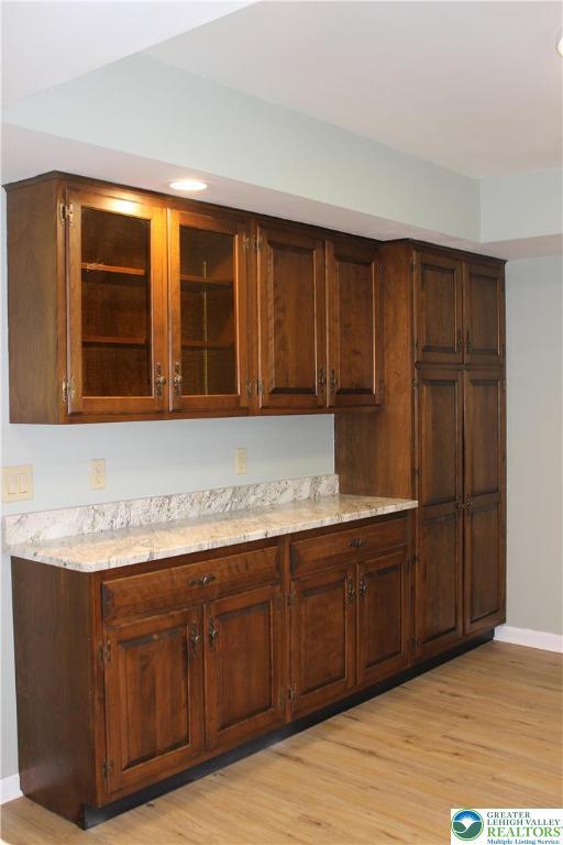 kitchen with light wood-style floors, baseboards, glass insert cabinets, light stone counters, and recessed lighting