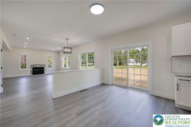 unfurnished living room featuring wood finished floors, baseboards, a chandelier, recessed lighting, and a high end fireplace