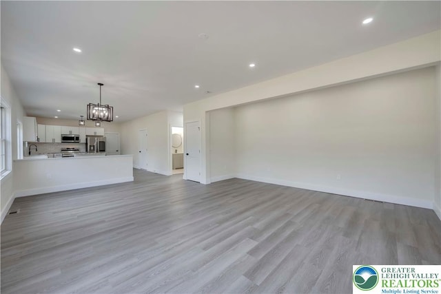unfurnished living room with recessed lighting, light wood finished floors, a chandelier, and baseboards