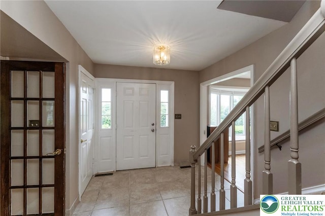 foyer entrance featuring light tile patterned floors, stairs, and baseboards