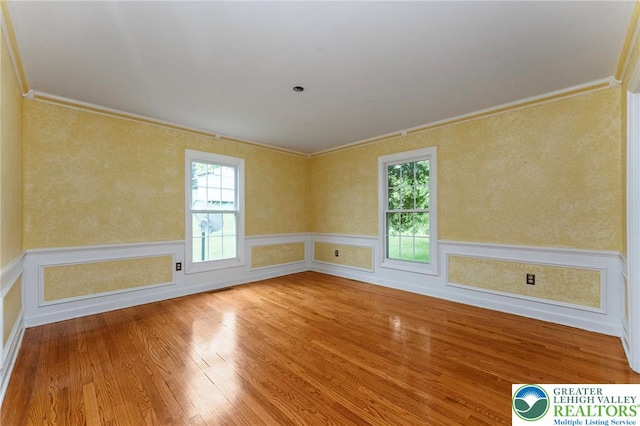empty room featuring crown molding, plenty of natural light, hardwood / wood-style floors, and a wainscoted wall