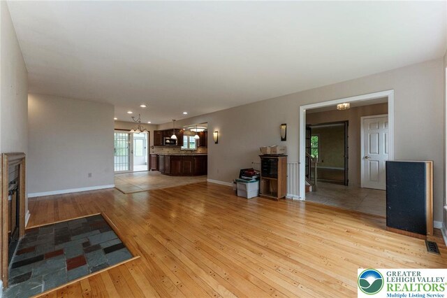 unfurnished living room featuring light wood-type flooring, recessed lighting, baseboards, and a chandelier