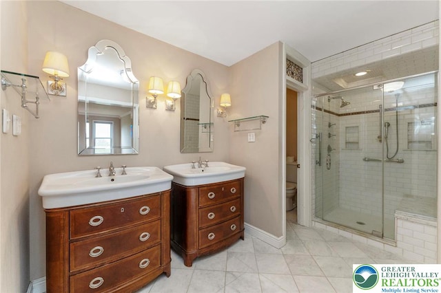 full bathroom with a stall shower, two vanities, toilet, baseboards, and tile patterned floors