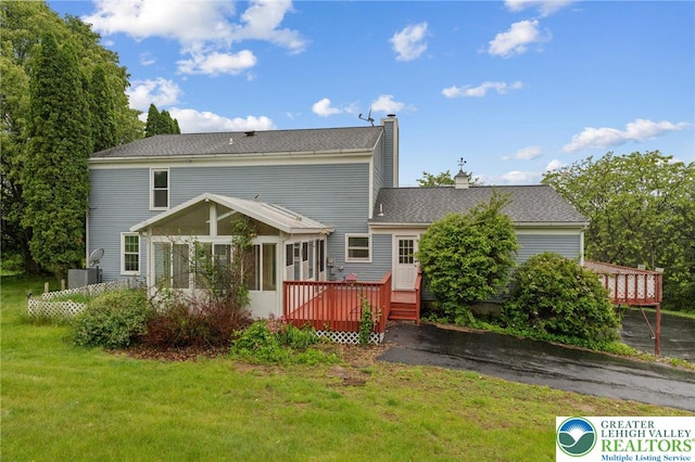 back of house featuring a wooden deck, a sunroom, a chimney, and a lawn