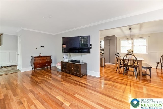 living room featuring light wood-style flooring, a decorative wall, crown molding, a wainscoted wall, and a chandelier