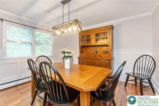 dining area featuring light wood-style flooring, a decorative wall, ornamental molding, a chandelier, and wainscoting