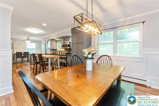 dining area featuring a baseboard radiator, ornamental molding, light wood-style floors, a decorative wall, and wainscoting