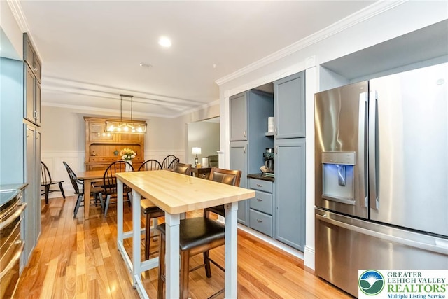kitchen with stainless steel appliances, ornamental molding, light wood-style flooring, a wainscoted wall, and pendant lighting
