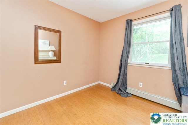 empty room featuring wood finished floors, baseboards, and a baseboard heating unit