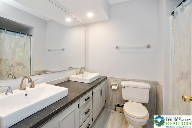 full bath featuring toilet, tile walls, a wainscoted wall, double vanity, and recessed lighting