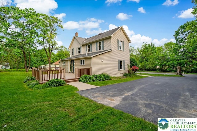 back of property featuring a chimney, a deck, and a lawn