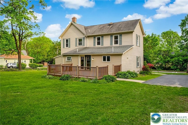 rear view of property with a chimney, a wooden deck, a yard, and a shingled roof