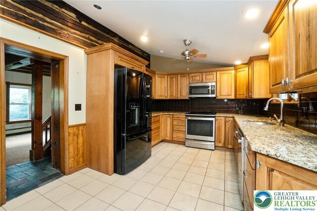 kitchen featuring appliances with stainless steel finishes, a sink, ceiling fan, a baseboard heating unit, and light stone counters