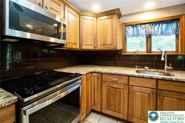 kitchen featuring appliances with stainless steel finishes, a sink, light stone countertops, light tile patterned floors, and tasteful backsplash