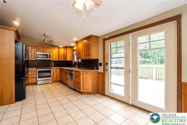 kitchen featuring appliances with stainless steel finishes, a ceiling fan, backsplash, brown cabinets, and light stone counters