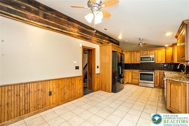 kitchen featuring stainless steel appliances, a sink, ceiling fan, wainscoting, and brown cabinets