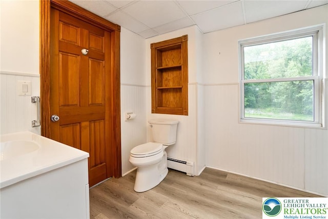 bathroom with toilet, wood finished floors, a baseboard radiator, wainscoting, and a drop ceiling