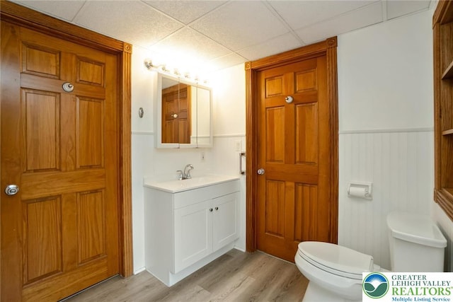 bathroom with toilet, wood finished floors, wainscoting, vanity, and a paneled ceiling