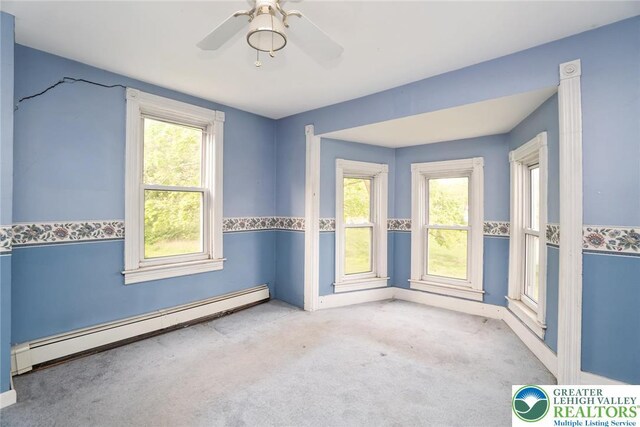 carpeted spare room with a baseboard radiator, a ceiling fan, and baseboards