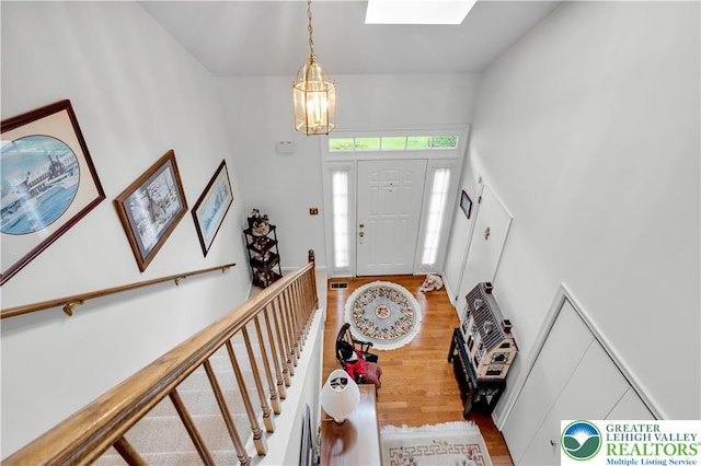 foyer featuring a chandelier, a skylight, wood finished floors, and a towering ceiling