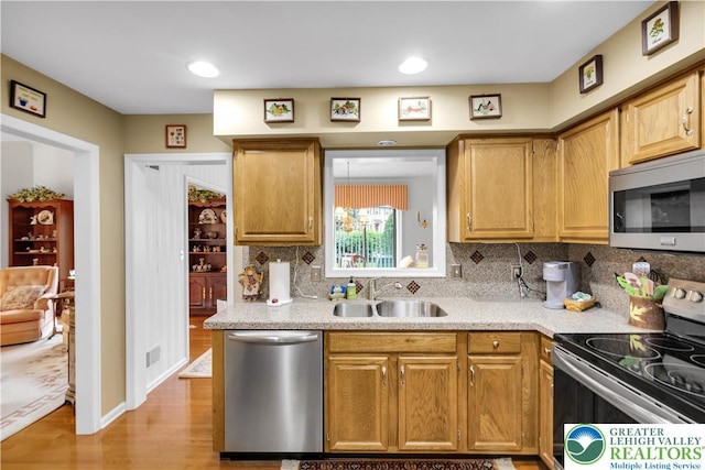 kitchen with stainless steel appliances, a sink, light countertops, light wood-style floors, and decorative backsplash