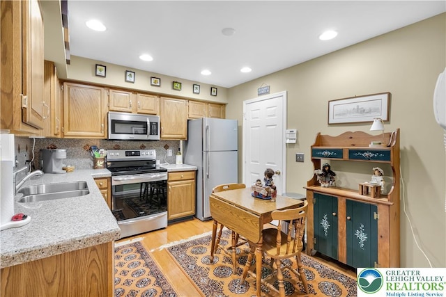 kitchen featuring appliances with stainless steel finishes, a sink, light countertops, light wood-style floors, and tasteful backsplash