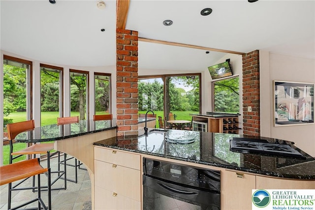 2342 Bobby Ct, South Whitehall Twp, PA 18069 - kitchen with lofted ceiling, dark stone counters, gas cooktop, black oven, and light brown cabinetry